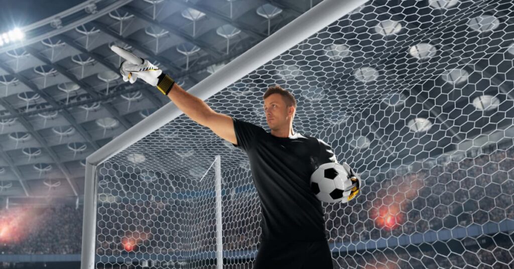 Portero moderno con balón dirigiendo la defensa dentro del área durante un partido profesional.