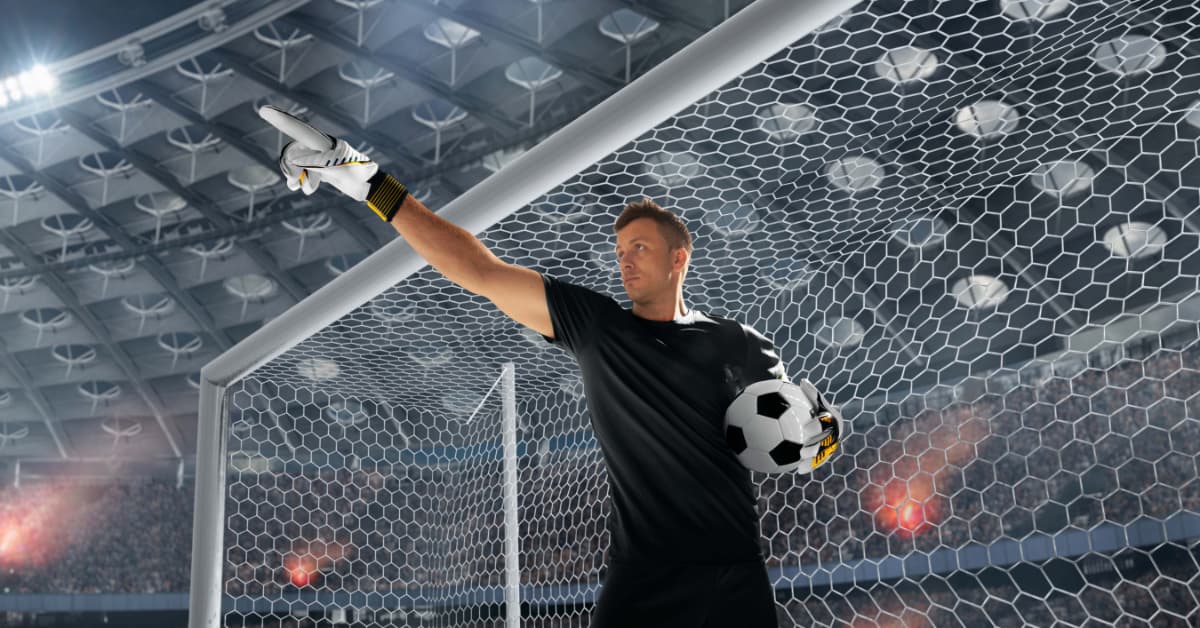 Portero moderno con balón dirigiendo la defensa dentro del área durante un partido profesional.