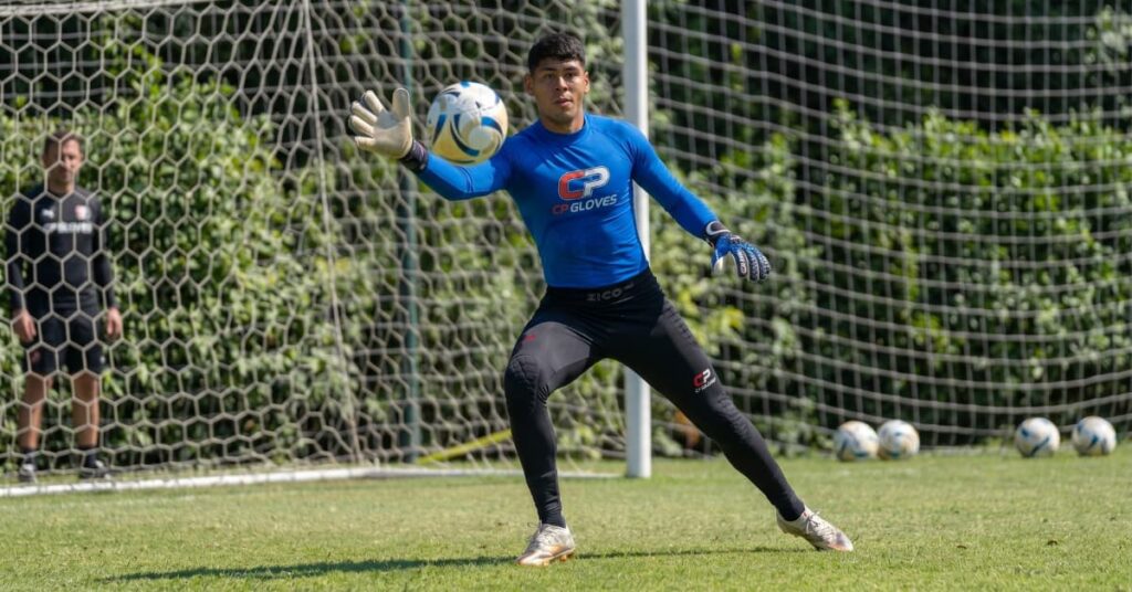 Portero de fútbol realizando un ejercicio de entrenamiento con guantes y equipamiento específico para mejorar la técnica de blocaje.